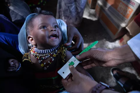 Seven months old Halima Amin smiles while a health worker measures her arm during a routine nutrition screening in Afar region