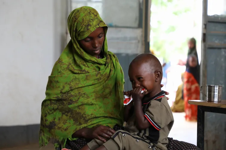 HIndia holding her baby Abdiwasa as he eats from RUTF pack