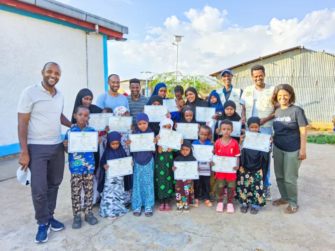 A group of children and mothers standing together for a group photo holding birth certificates