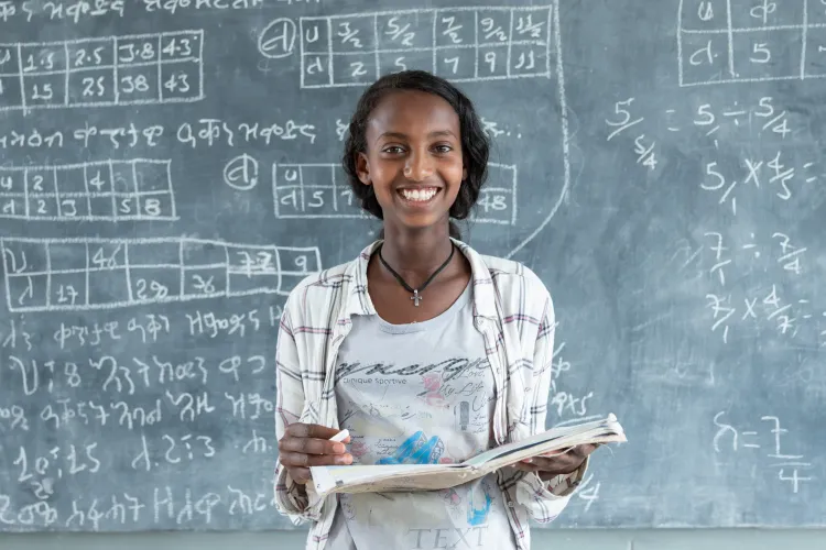 A young girls smiles holding her book in font of class