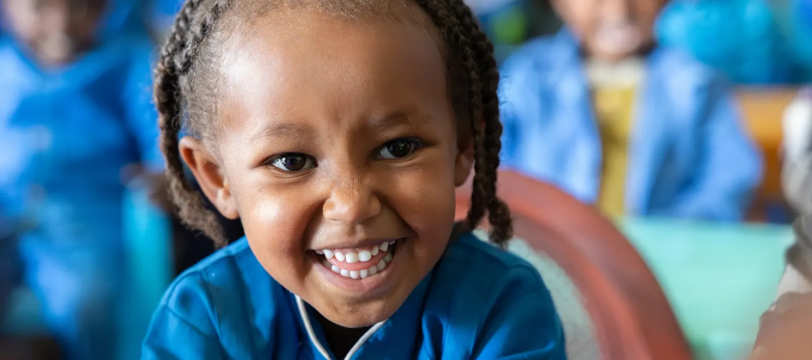 A little girl sitting in her classroom and smiling for the camera