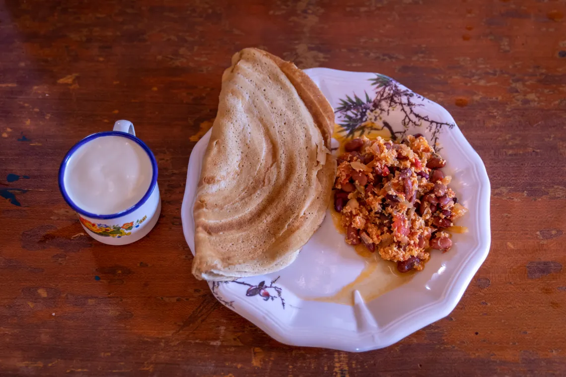 Milk in a mug and next to it is a plate with flat bread and cooked beans.