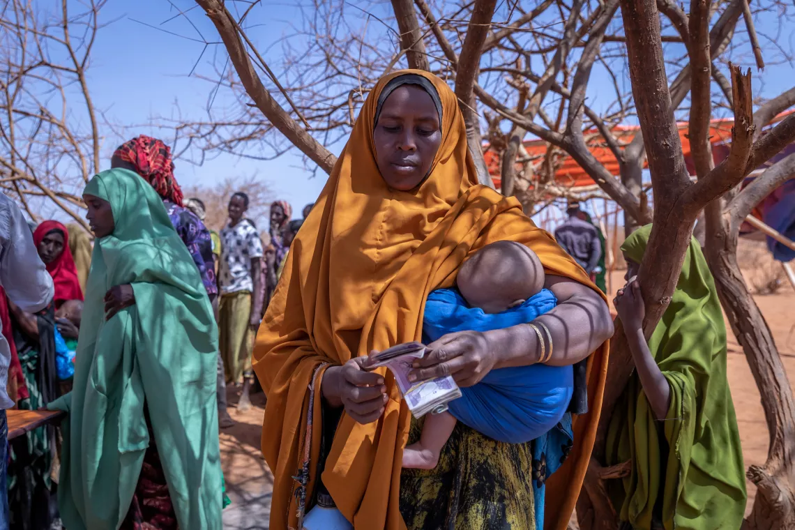 Arish counting money while holding her infant child.