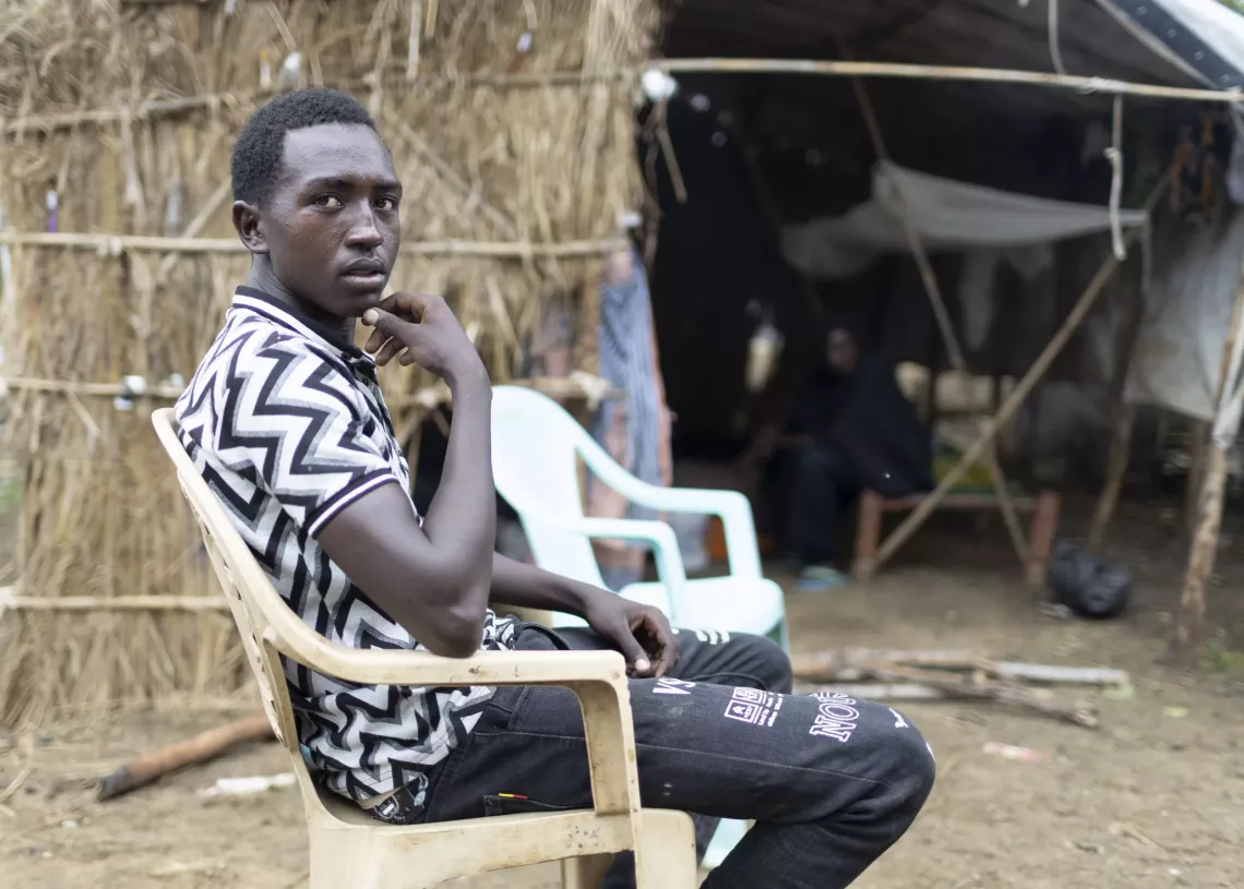A young man sitting on a chair and looking back at the camera. 
