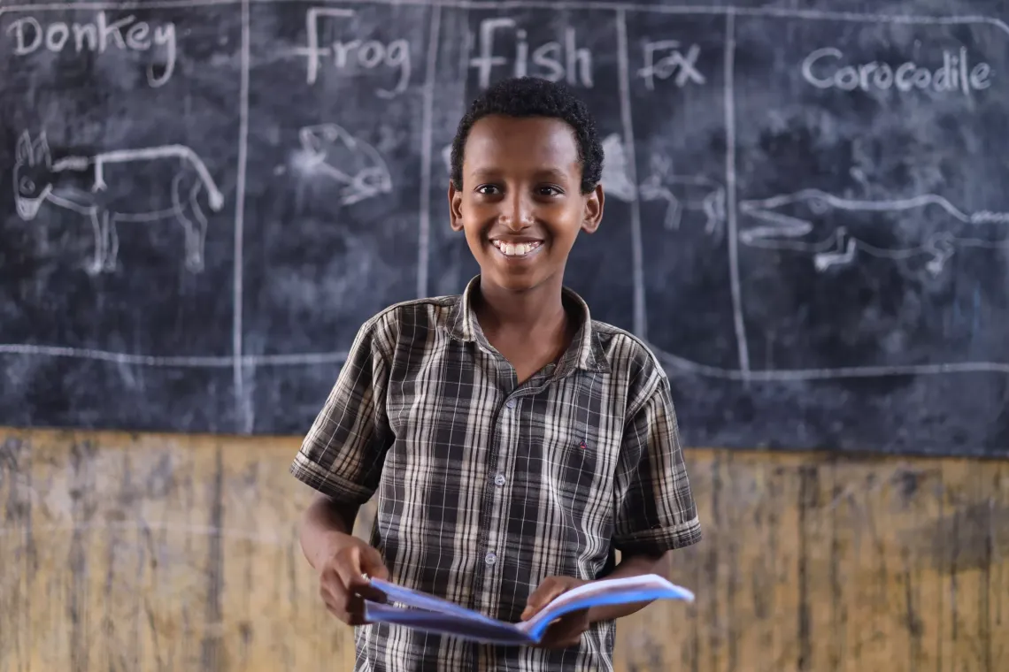 A child standing infront of his class holding his exercise book