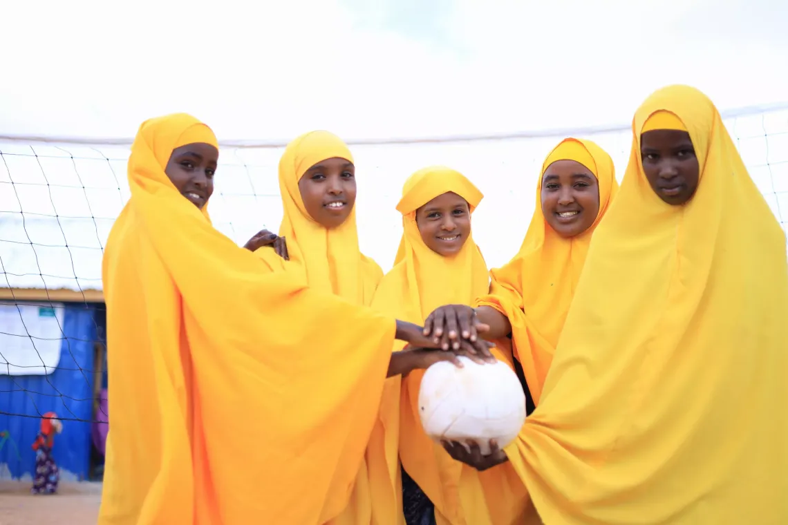 A group of adolescent girls outside a SPEED school's volleyball field holding hands over a volleyball