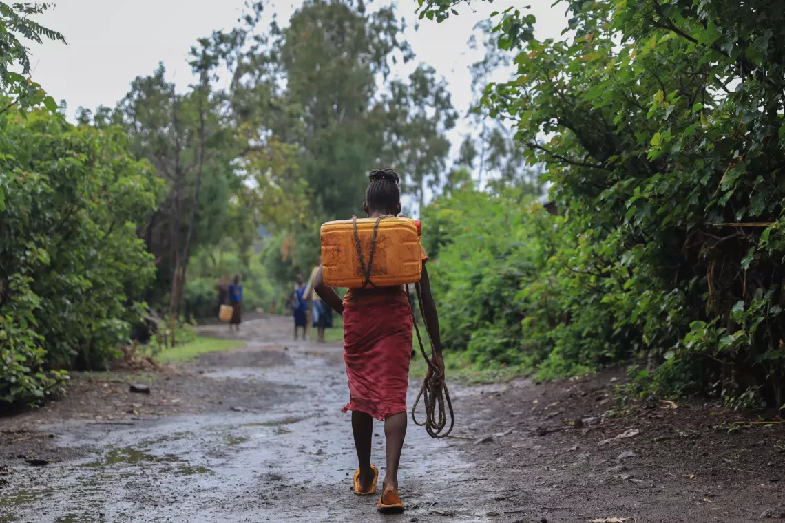 A young girl walk carrying a jerry can of water. 