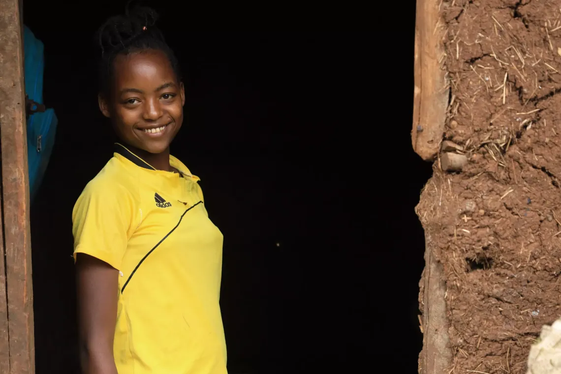 A girl standing next to her house smiling. 