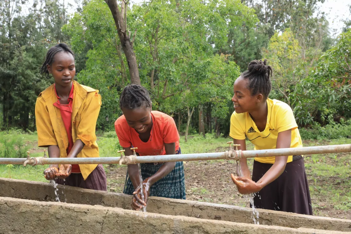 Three young girls smile as they wash their faces. 