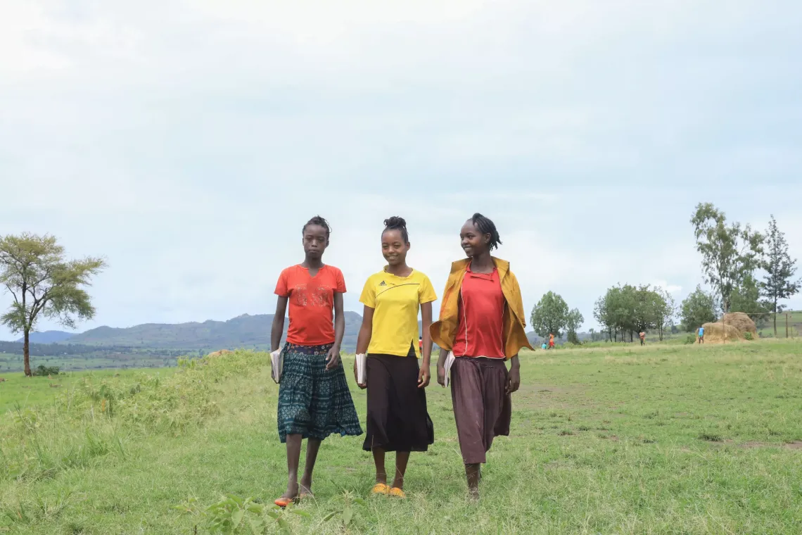 Three young girls waking to school carrying books. 