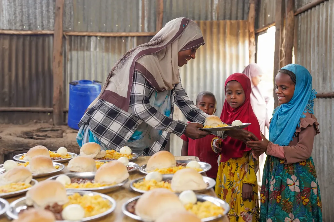A female teacher gives children school meals on a plate.