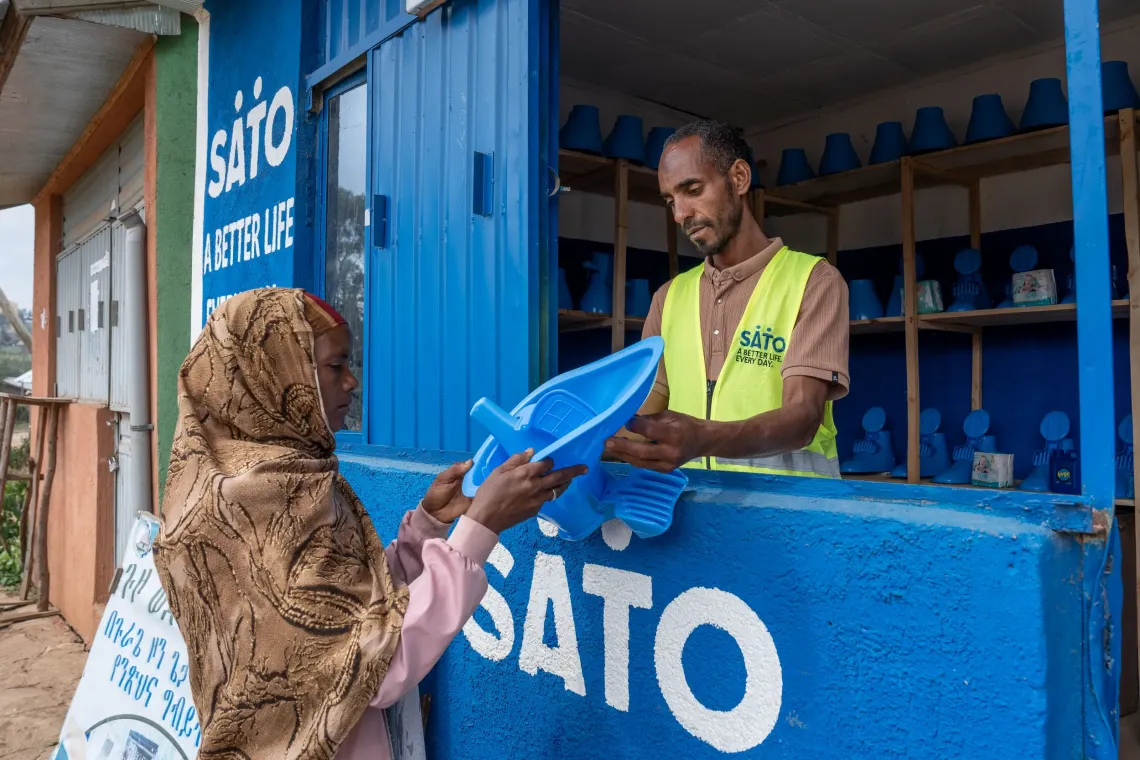 A young man standing inside his sanitary shop and selling a sanitary product to a women 