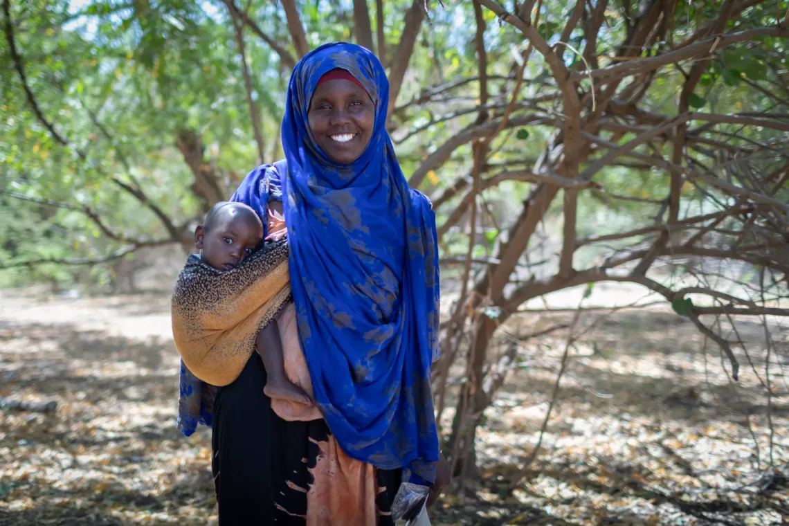 A mother standing outside and posing for the camera while holding her baby by her side