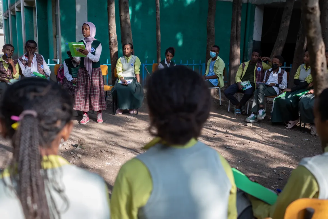 A young female reading out loud for students sitting in circle