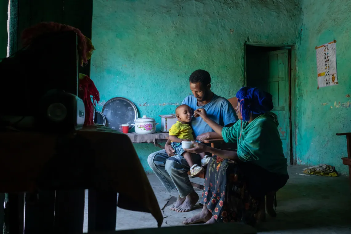A mother feeds her child while her husband holds the baby
