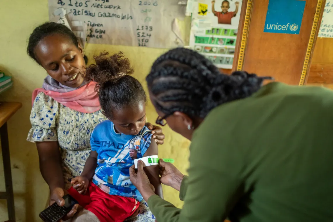 A child sits on her mom's lap while her MUAC is being measured 