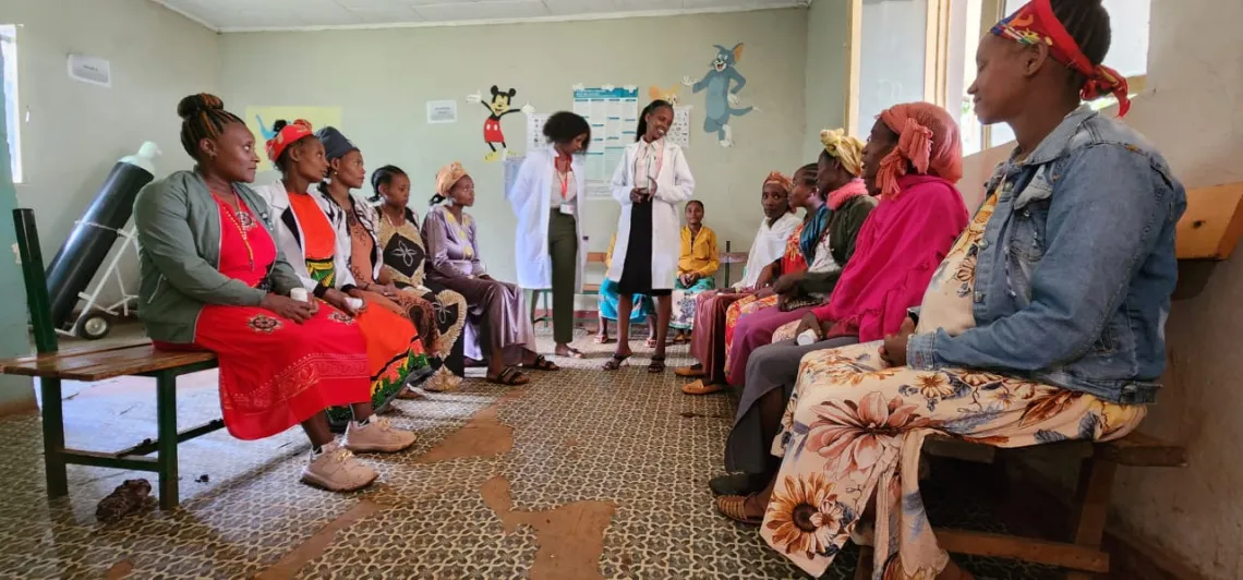 12 pregnant women sitting and two health workers standing at a health center during a pregnant women&rsquo;s counseling session. 