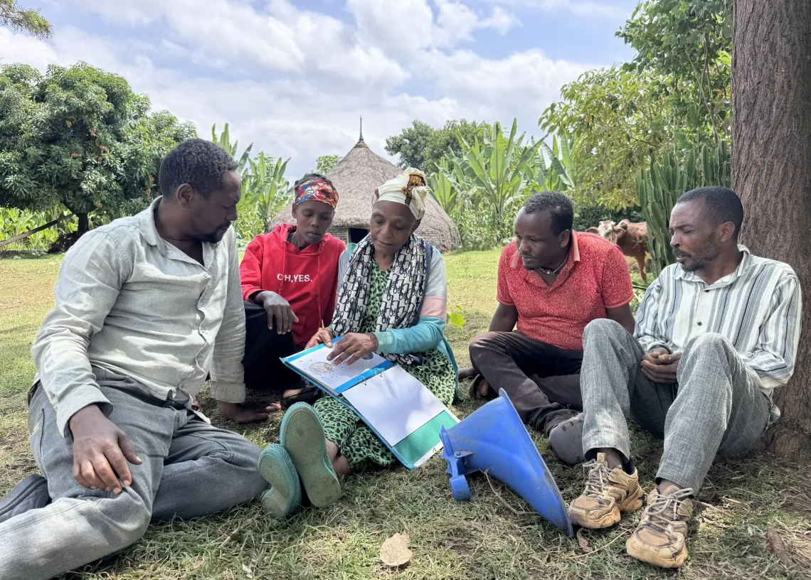 A women sitting on the ground with three men and one women, and explaining about the products her enterprises is producing