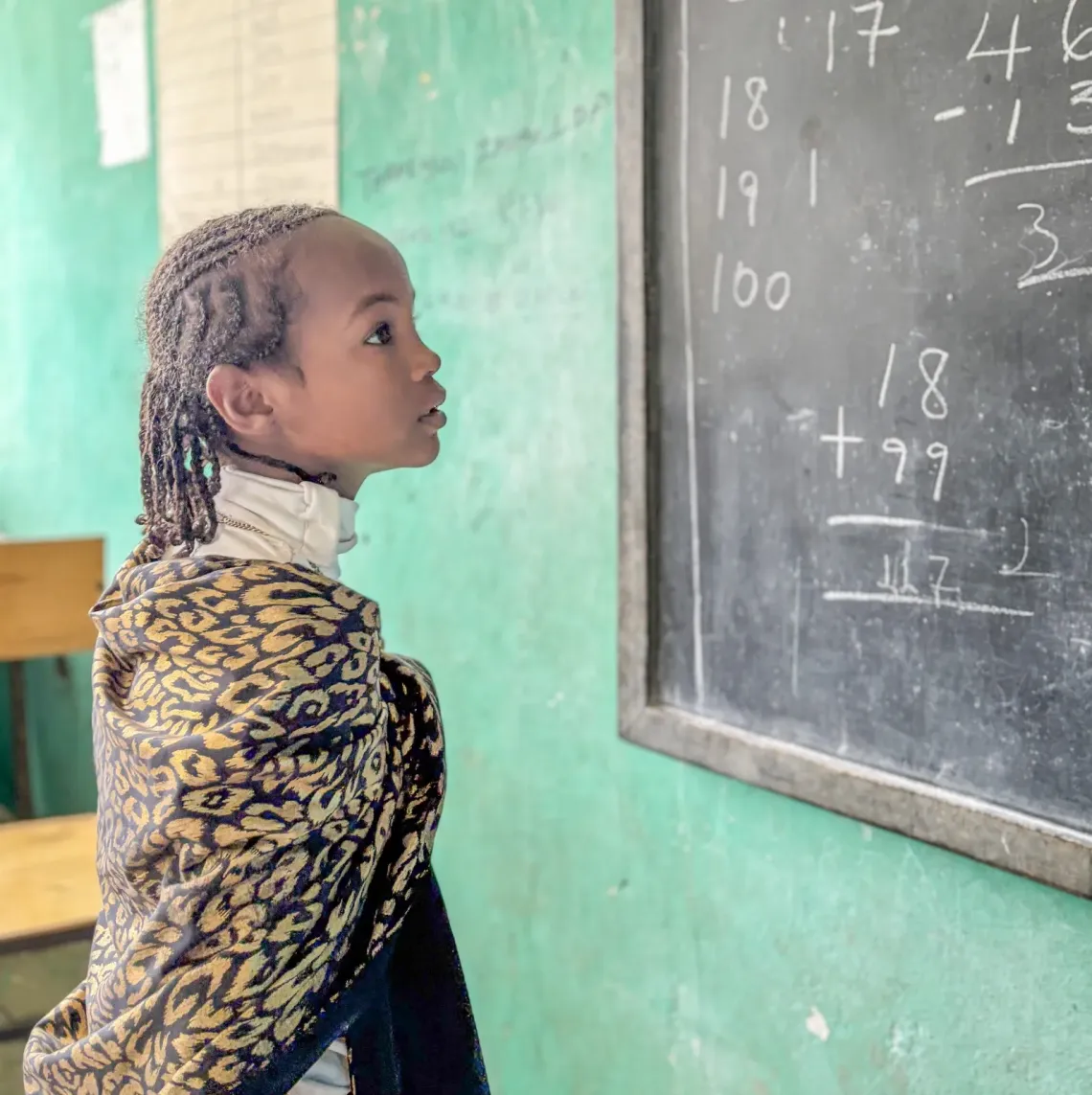 A little girl standing in front of a black board