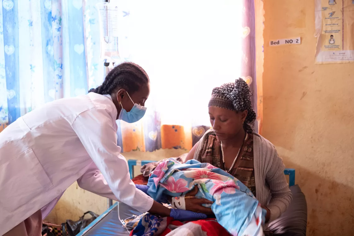 A health worker giving a newly born baby to the mother and showing her how to hold him