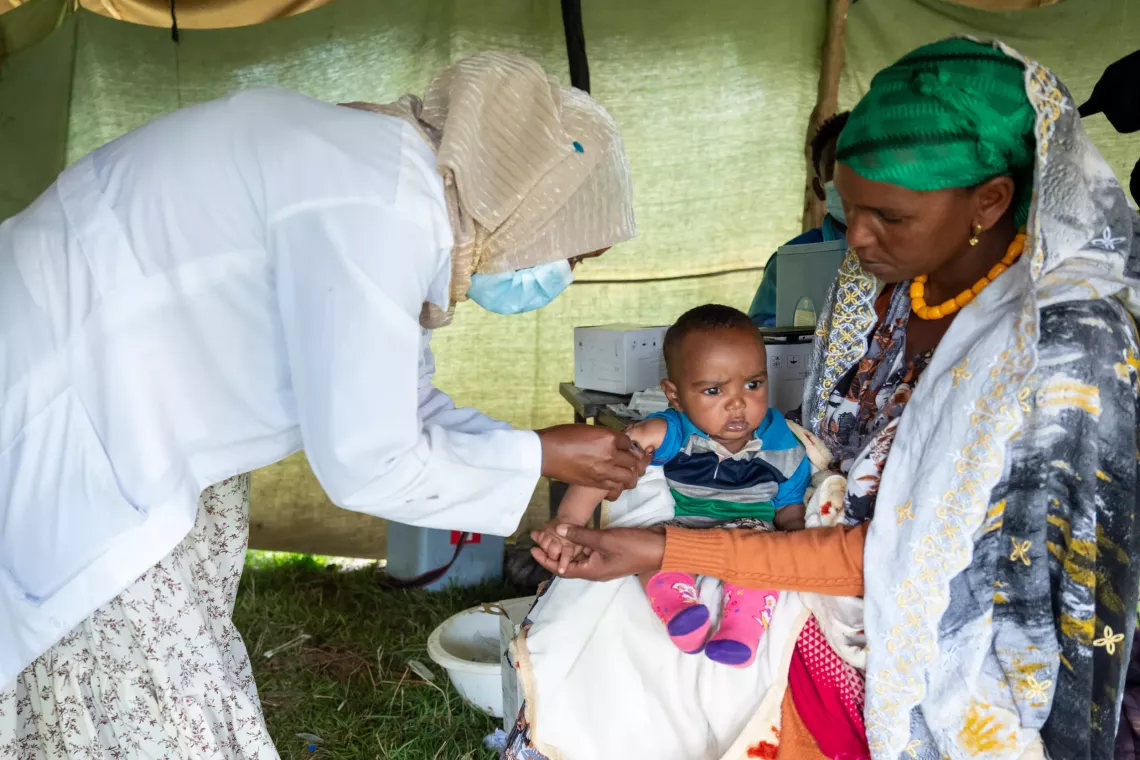 A mother holding her son, while a health worker is getting ready to give him a vaccine. 