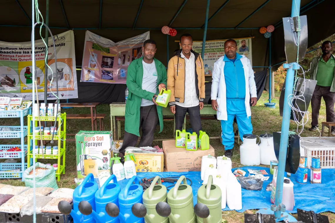Three men wearing uniforms and showing WASH equipment for the camera. 