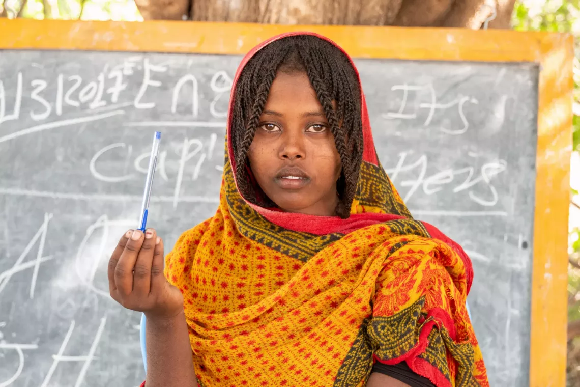 An adolescent girl pausing for a photo while holding a pen in her hand