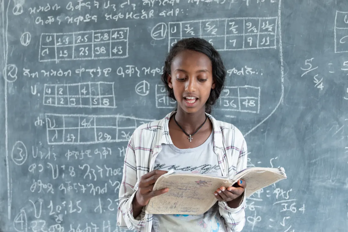 A young girl reads from her book in front of calss