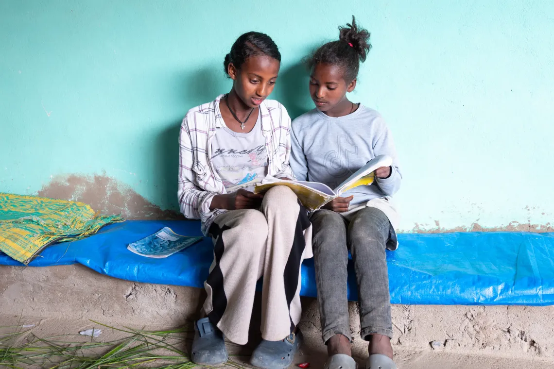 A girl sits with her younger sister and help her read from a book