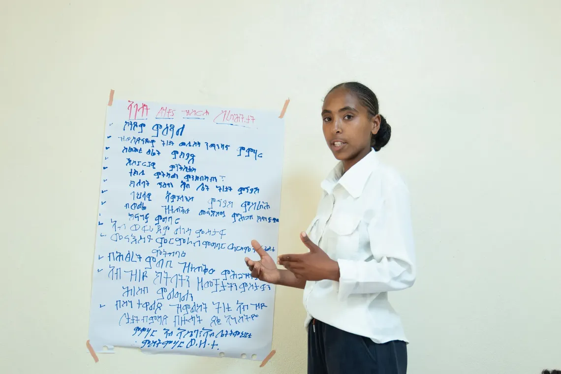 A young girls make a presentation with a chart mounted on a wall. 