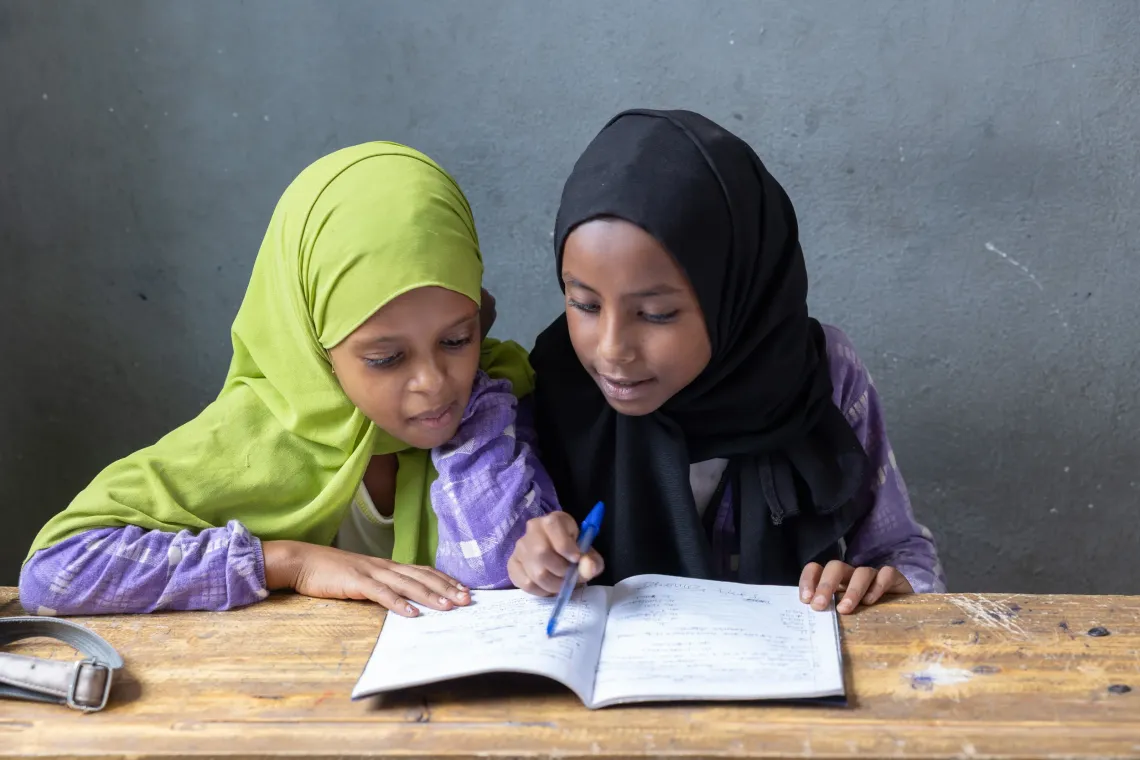 Two girls wearing hijab and reading one book together 