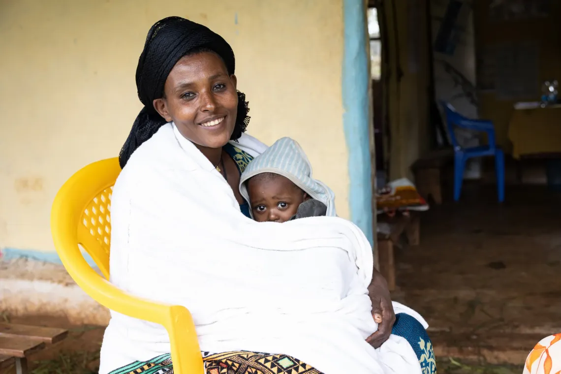 A mother sits holding her three year old daughter. 