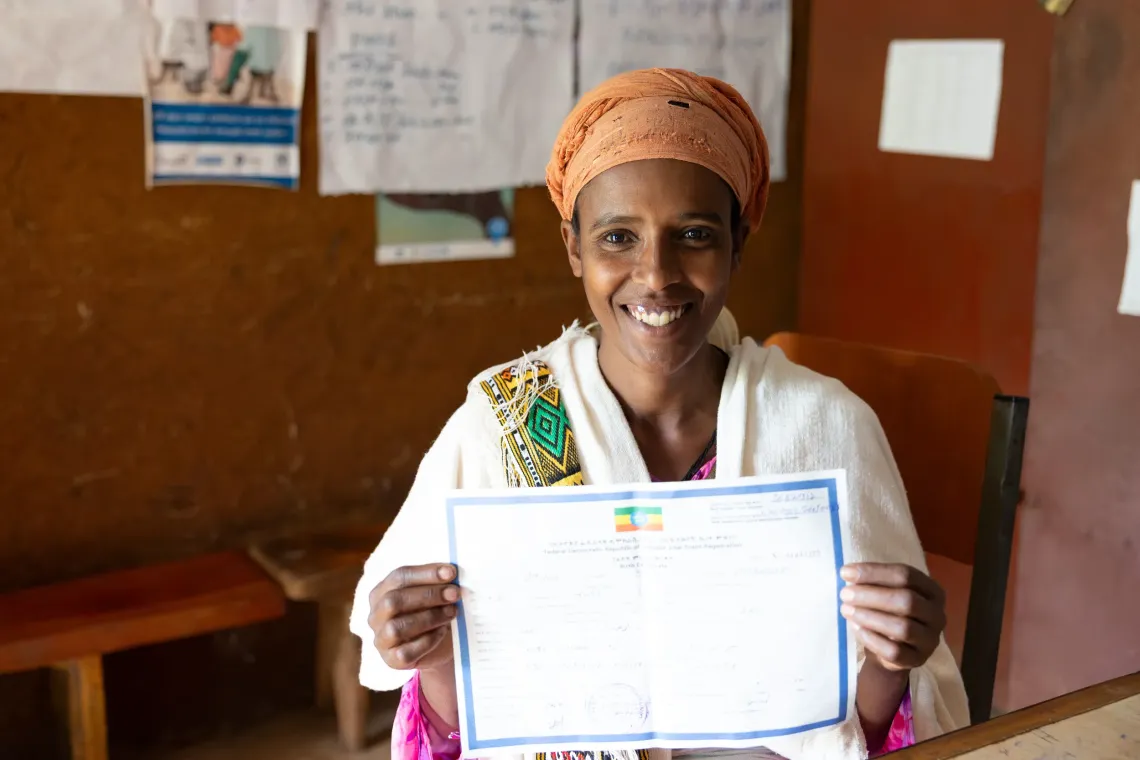 A mother smiles holding her child's birth certificate. 