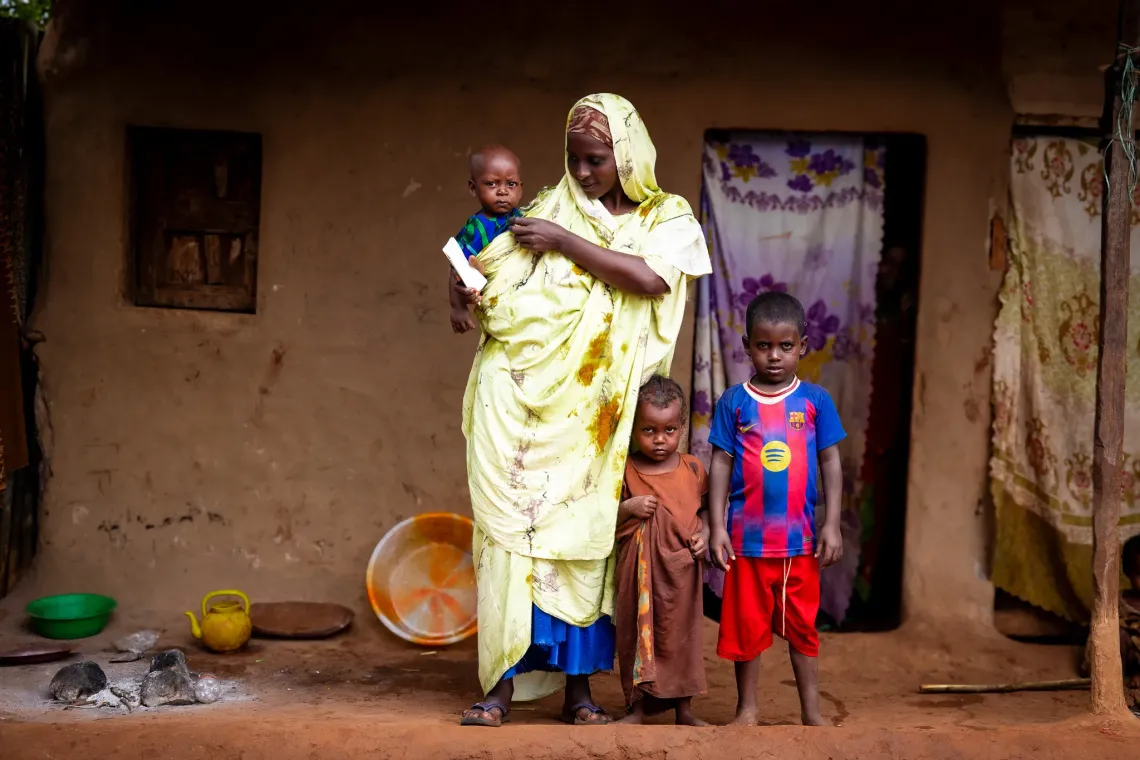Teyiba holding her youngest child and posing with her two other children infront their home