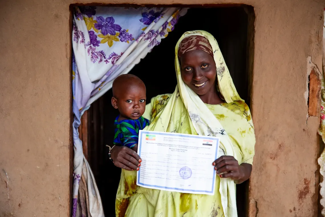 Teyiba posing while holding held child and her child's birth certificate
