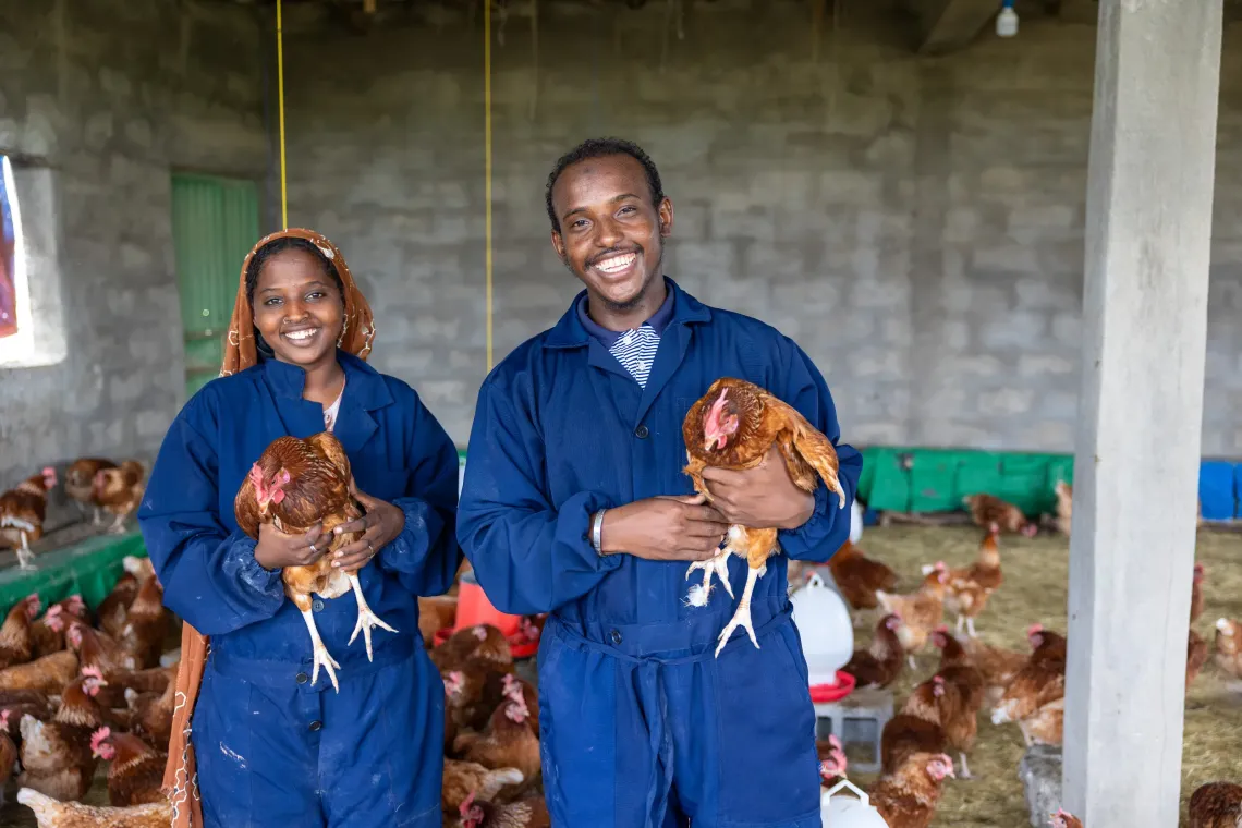 A young woman and young man smile to the camera holding chicken in their poultry farm