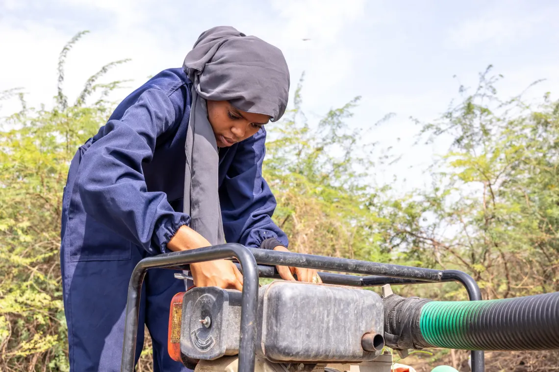 a young women wearing a jump suite fixing a water pump.