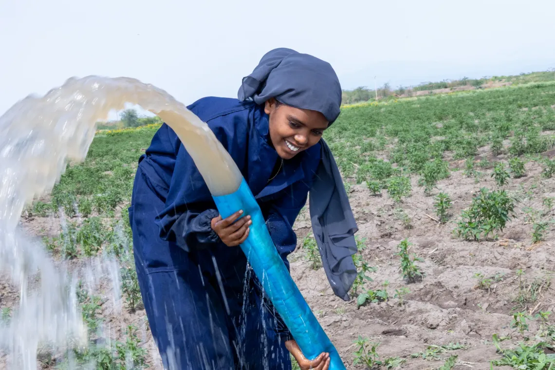 A young women smiles while holding a bit water hose and water flowing intensely. 