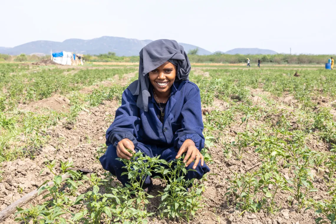 a young women sits inside a vegetable farm smiling 