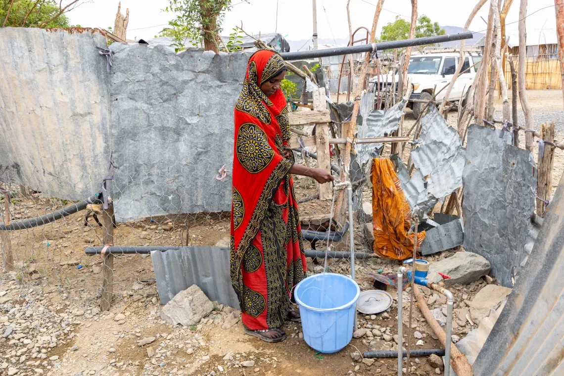 Woman in red dress fetching water from a tap.