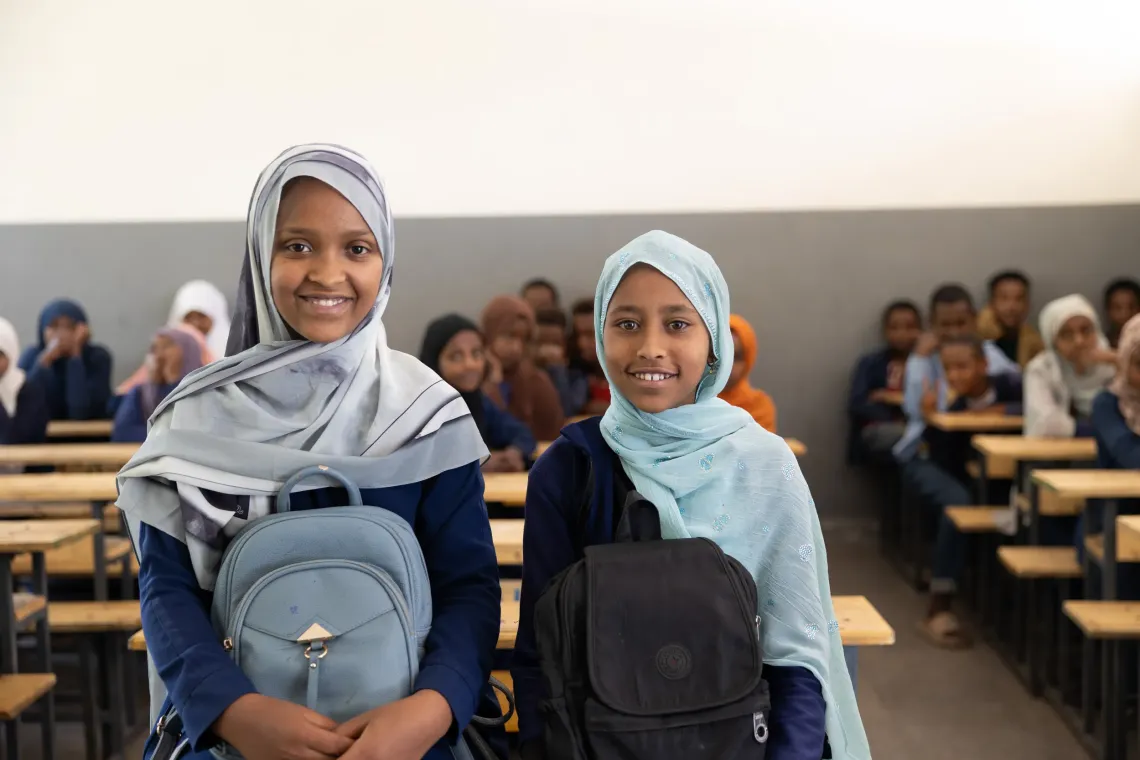 Adolescent girls smile to a camera holding their schoolbags 