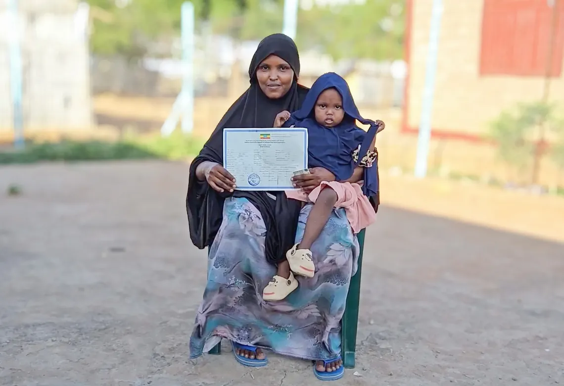 A mother sits holding her daughter and her child's birth certificate. 