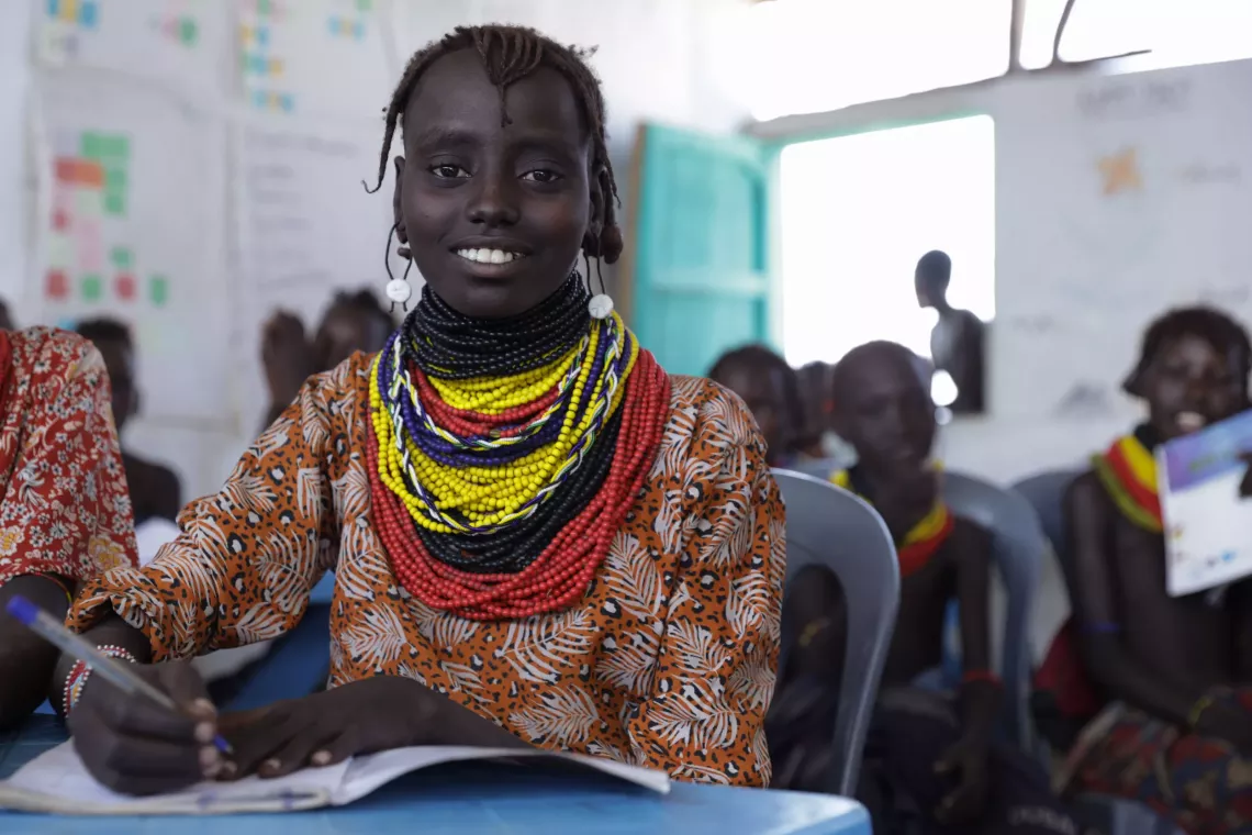 Young girl sitting in her classroom and writing on her notebook
