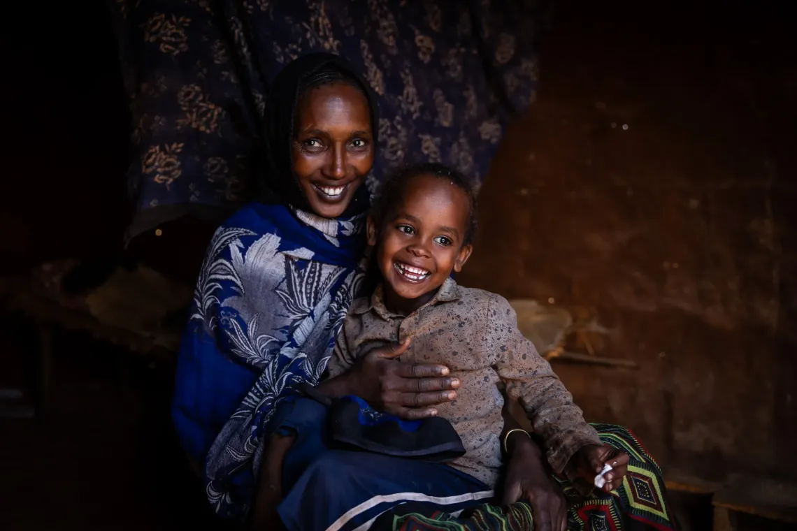 A mother and her baby boy, sitting on the floor and smiling for the camera