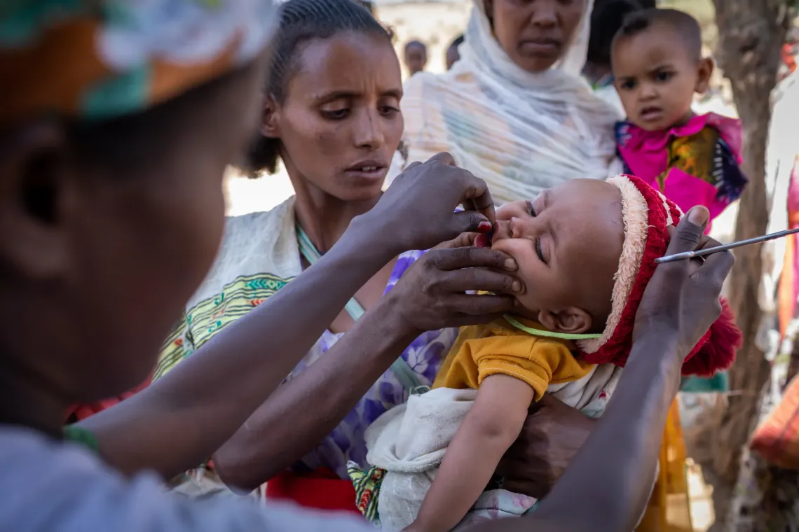 A mother holding her baby while a health worker give the baby Vitamin A