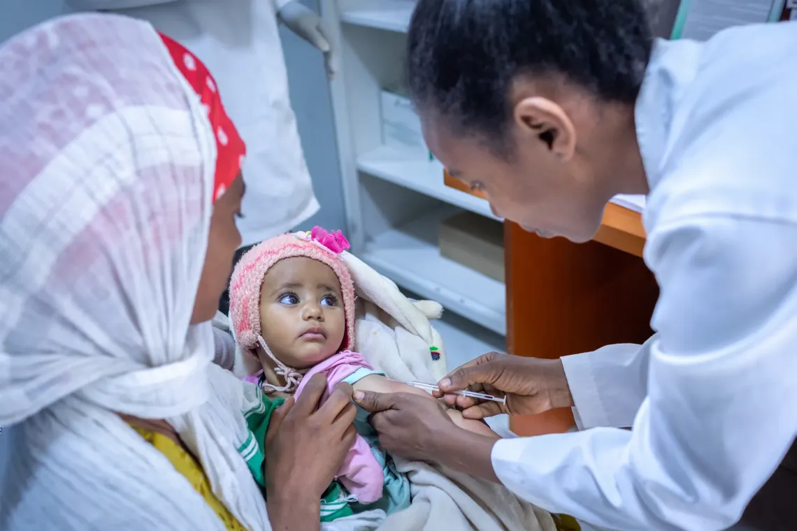 A mother holding her baby, while she receives measles vaccine