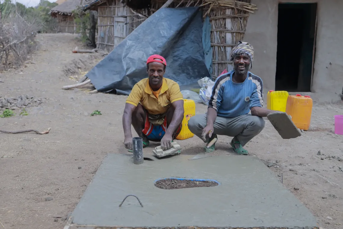 Two men producing precast latrine slabs
