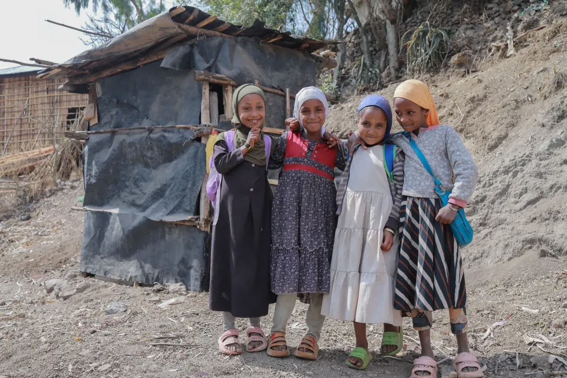 Four little girls standing together with their back bags on and smiling for the camera