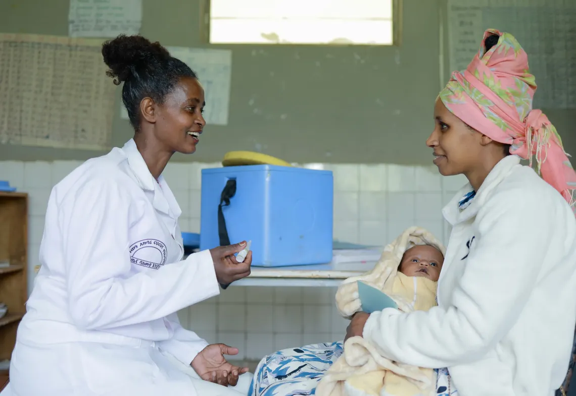 A mother holding her baby in her hand while the health worker gets ready to give her vaccine