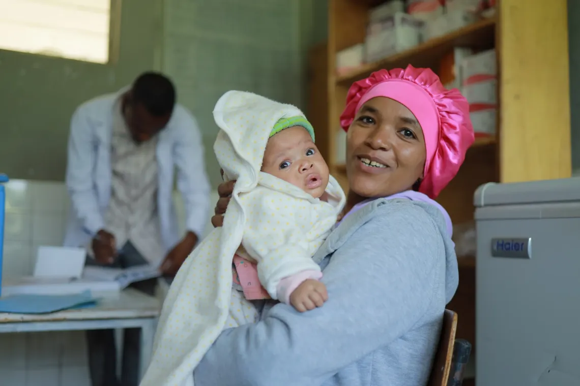 A mother holding her baby in her arm and smiling at the camera
